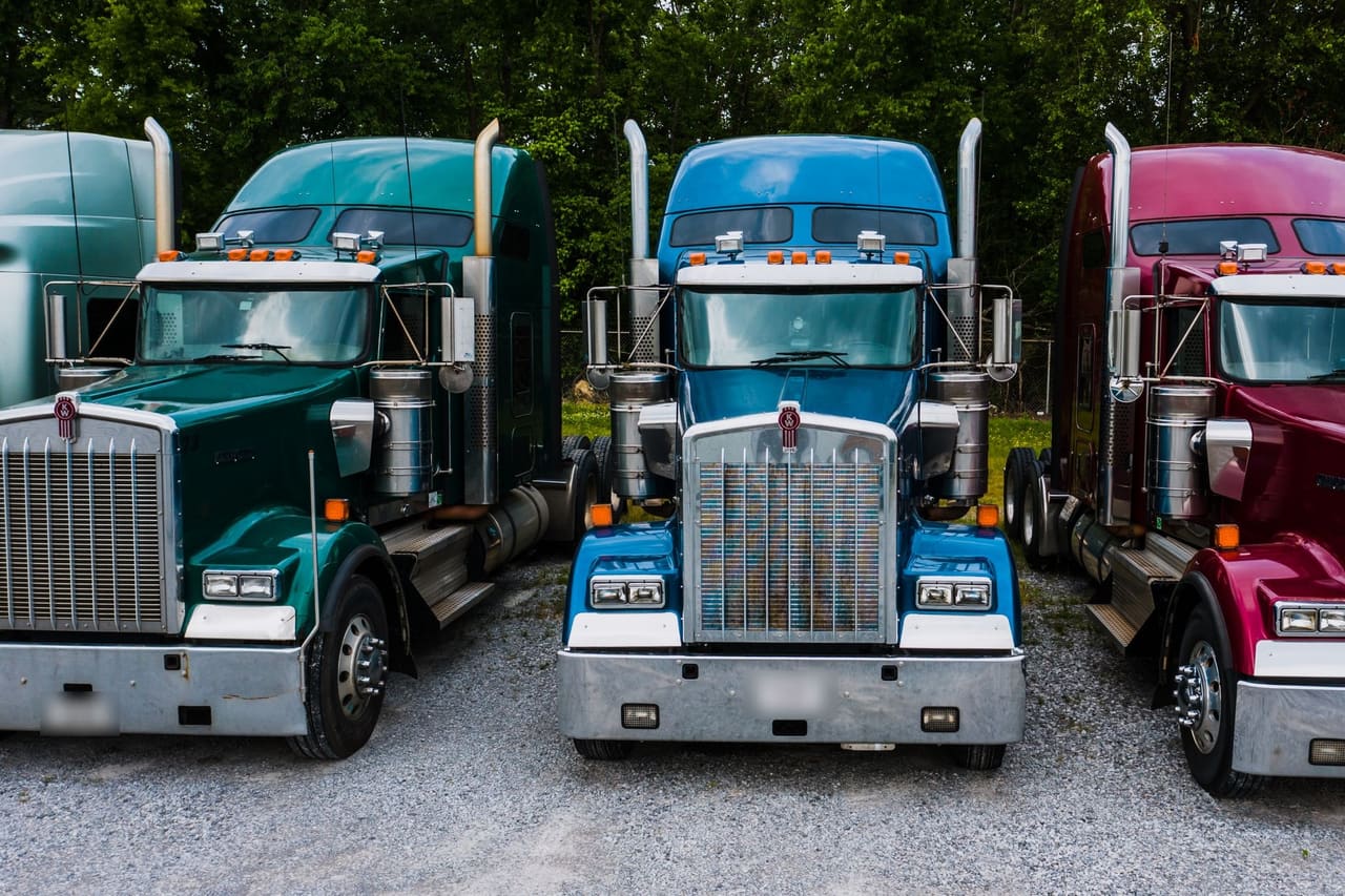Three semi truck tractors parked side by side on a gravel yard.