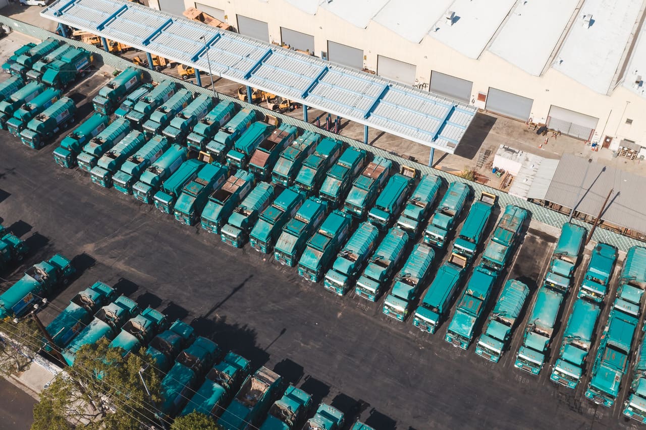 A fleet of trucks parked in rows beside a depot, seen from above.